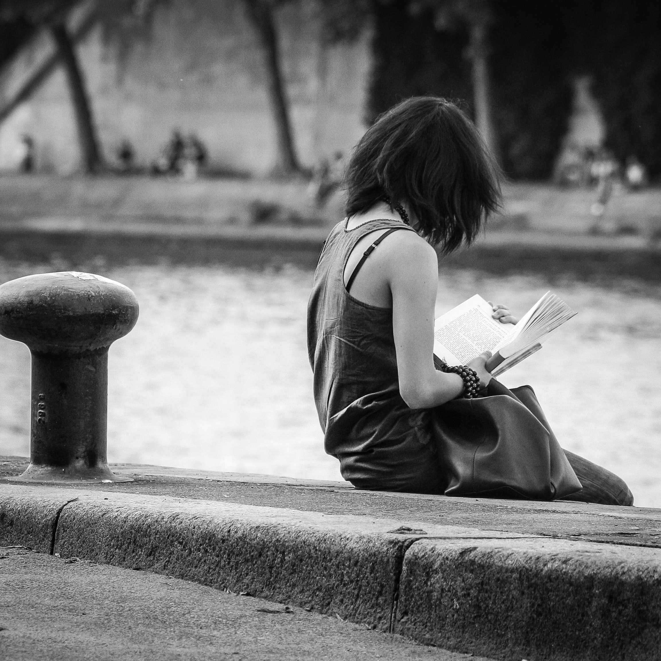 Outdoors by park fountain young woman reads open book
