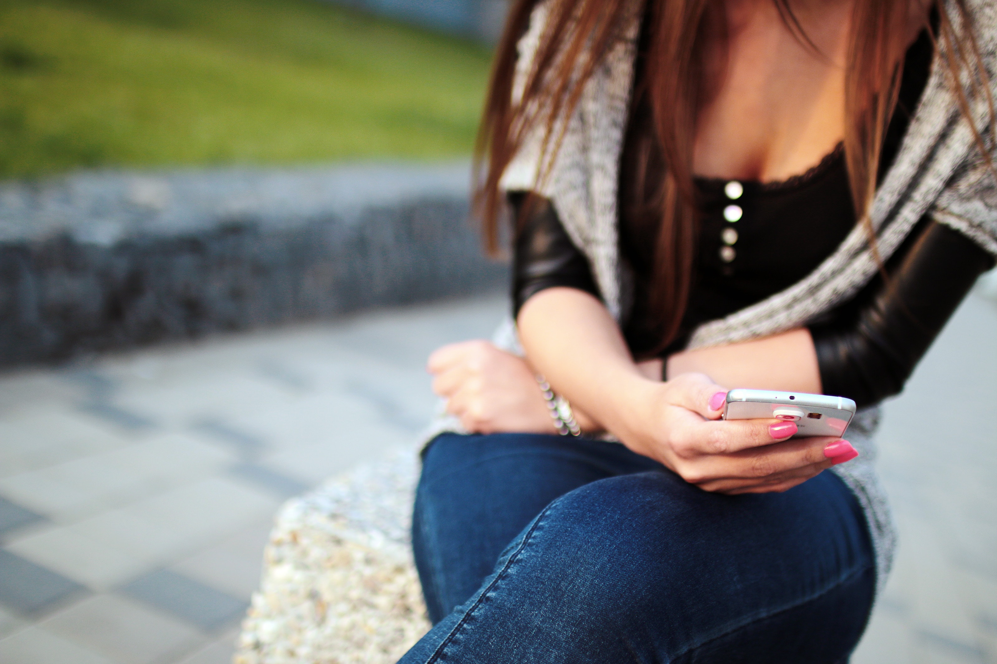"Satisfying too" - Young woman examines her cellphone, seated outside